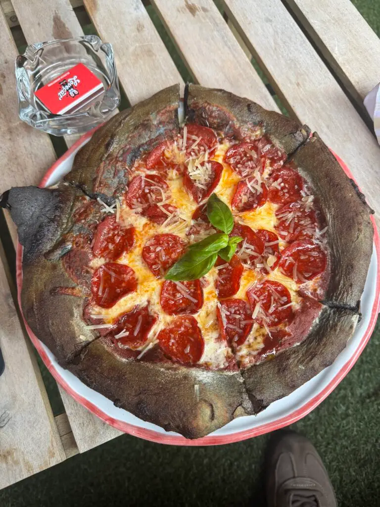 Pepperoni pizza with fresh basil on a tray at an outdoor table